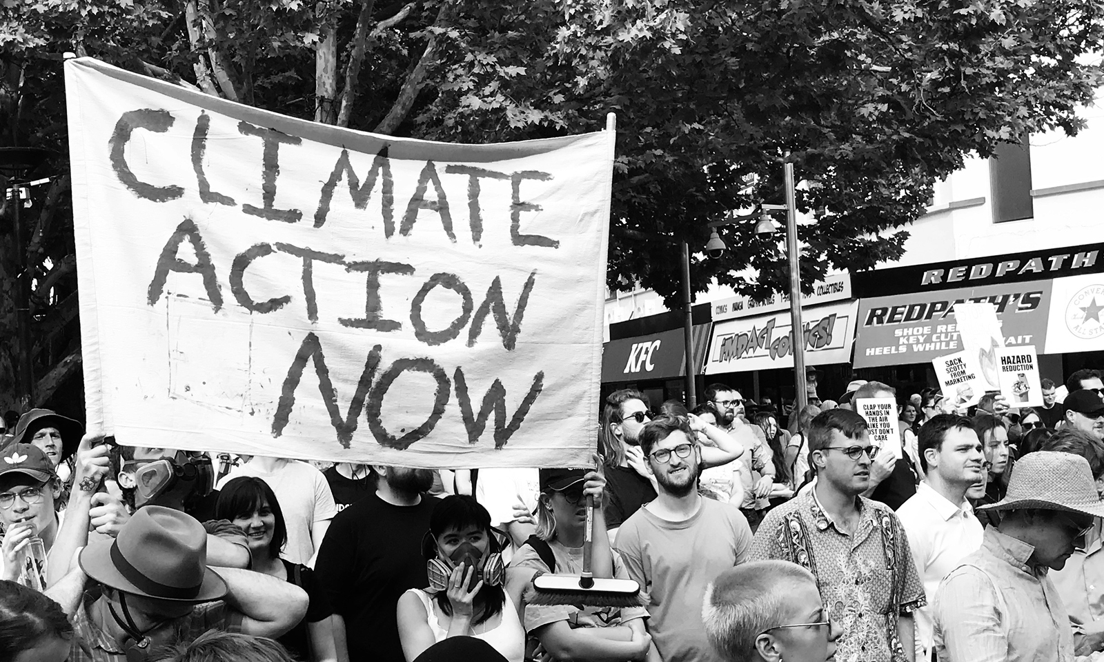 Čiernobiela fotografia ľudí na klimatickom proteste, držiacich transparent s nápisom 